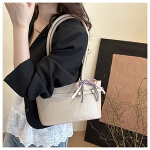 Detail of cream shoulder bag with pink and checkered bow decoration on side