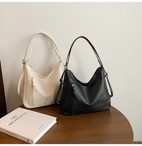 Detail view of large minimalist hobo bags in black and beige on a wooden table