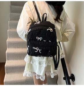 Detail of black quilted backpack featuring colorful embroidered bows and leather handle