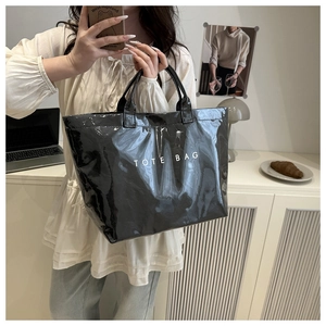 Close-up of a large black glossy PVC tote bag with white TOTE BAG text print