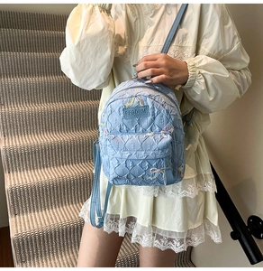 Close-up of light blue quilted mini backpack with embroidery details and zipper pocket
