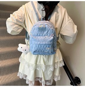 Close-up of light blue quilted backpack with rainbow embroidery and plush cloud charm