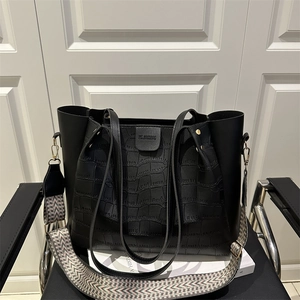 Black crocodile pattern tote bag with woven shoulder strap on a black leather chair