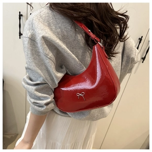 Detail of red patent leather hobo bag featuring a silver metal bow and shoulder strap