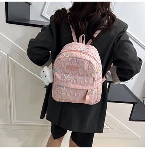 Detail of pink quilted backpack featuring colorful butterfly embroidery and plush charm