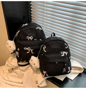 Detail of two black nylon backpacks with sequined bows and white cloud plush charms
