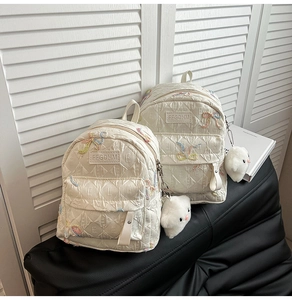 Macro shot of white quilted mini backpack with embroidery and plush cloud charm