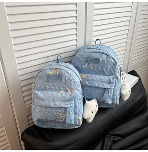 Detail of light blue nylon backpack with diamond quilting and embroidered bows