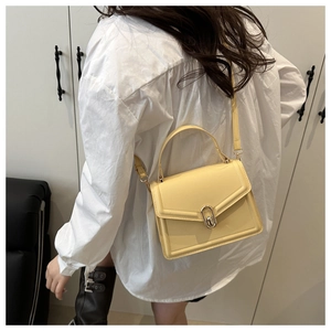 Detail van een crèmegele crossbodytas met gouden gesp gedragen op een wit overhemd