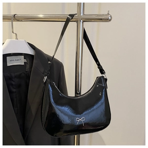 Detail of black patent leather crescent bag with silver bow hardware hanging on a rack