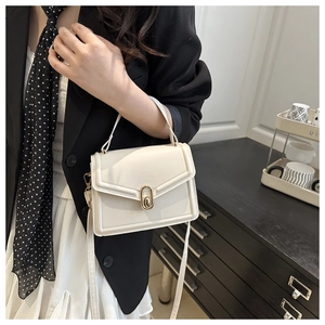 Detail van elegante gebroken witte tas met een goudkleurige ovale draaisluiting