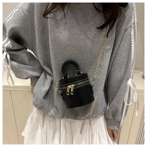 Close-up of a black mini bucket bag with gold zippers and chain strap on a model