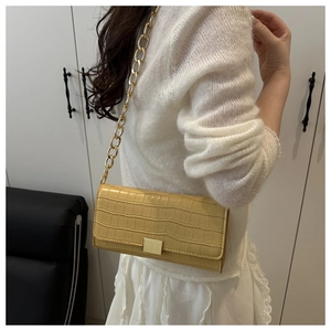 Detail view of yellow croc-pattern baguette bag with chunky gold chain strap on model