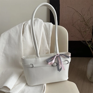 White minimalist PU leather tote bag with a decorative ribbon bow on a stylish chair