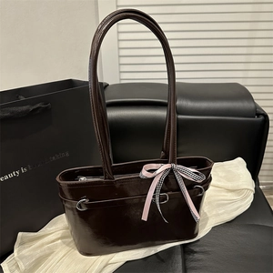 Deep brown glossy retro shoulder bag with bow detail on a leather sofa backdrop