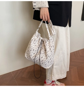 Detailed close-up of a floral drawstring bucket bag in beige with purple flower patterns