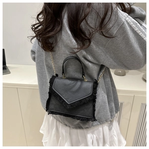Détail d'un mini sac carré noir avec bordures à franges et bandoulière chaîne dorée