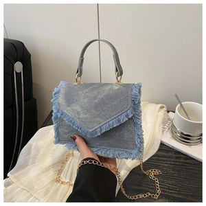 Détail du sac en denim bleu clair avec franges, rabat en V et bandoulière dorée