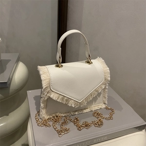 Sac bandoulière blanc crème avec chaîne dorée et bords frangés sur décor minimaliste