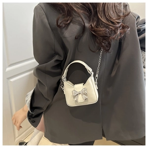 Detail of a mini cream-white crossbody bag with a metallic silver bow on a grey suit