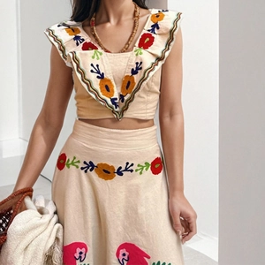 Detail of bohemian two-piece set with floral embroidery and ruffle trim on beige linen