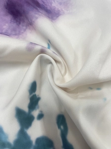 Detailed close-up of soft white tie-dye fabric with purple and blue-green marbling texture