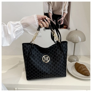 Detail of black tote bag with M-pattern monogram, gold logo and chain strap handle