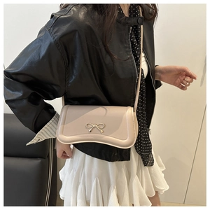 Model wearing a cream faux leather baguette bag with a stylish gold bow metal clasp