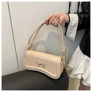 Close-up of beige leather crossbody bag with golden bow clasp and knot strap detail