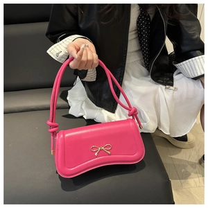 Close-up of rose red crossbody bag with golden bow clasp and stylish knotted shoulder strap