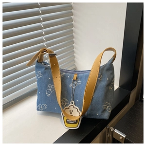 Detail of light blue denim shoulder bag featuring cartoon print and leather strap
