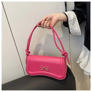 Close-up of a pink shoulder bag featuring a decorative gold metal bow on the front flap