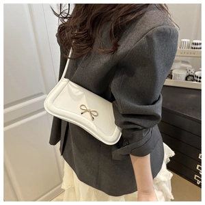 Detail of white glossy faux leather shoulder bag with a gold metal bow on a model