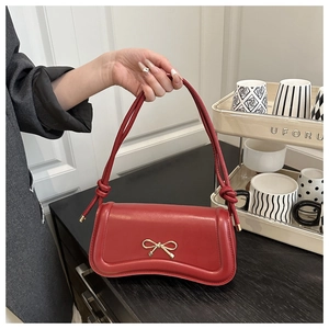 Detail of red curved handbag featuring a golden bow metal buckle and knotted handle