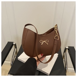 Detail of a brown shoulder bag featuring a gold bow clasp and metallic chain strap