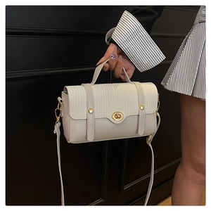 Detail van beige crossbodytas met geweven textuur, gouden studs en metalen draaislot