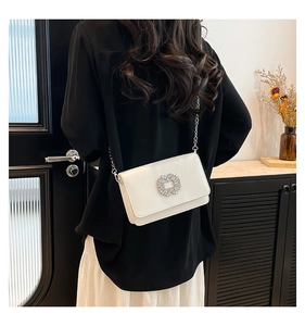Detail of white glossy square bag with rhinestone buckle and silver chain on model
