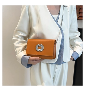 Detail of orange crossbody bag featuring a sparkling rhinestone buckle and silver chain