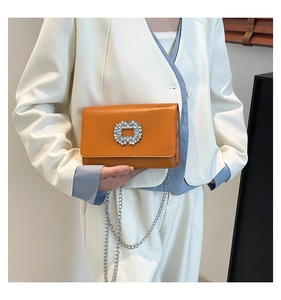 Detail of bright orange crossbody bag featuring a sparkling rhinestone buckle and silver chain