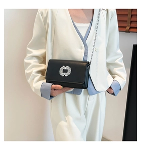 Detail of elegant black leather flap bag with sparkling rhinestone buckle on a white blazer