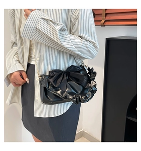 Detail of black pleated shoulder bag featuring a large bow and elegant gold chain strap