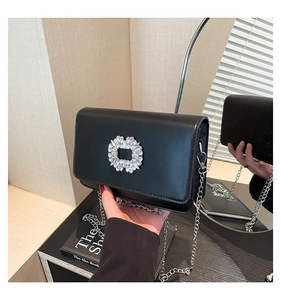 Detail shot of black leather handbag featuring a sparkling rhinestone square buckle and chain