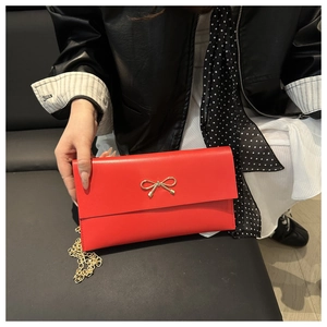 Vue macro d'une pochette rouge rectangulaire avec fermoir nœud doré et bandoulière chaîne