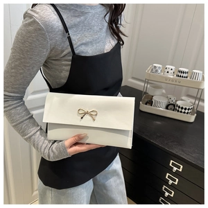 Détail d'une pochette enveloppe blanche avec nœud doré tenue par un mannequin