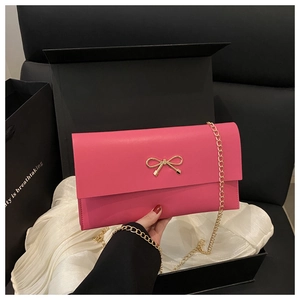 Close-up of rose pink envelope bag featuring a golden bow buckle and chain strap in a gift box