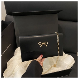 Detail of black crossbody bag with gold bow ornament and chain in gift box packaging