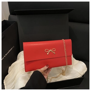 Detail of red leather clutch bag with golden bow and chain in a premium black gift box