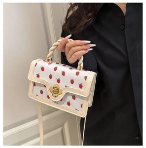 Detail of strawberry print square bag with golden petal buckle and woven handle