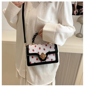 Detail of strawberry print crossbody bag with golden rose clasp worn by a model