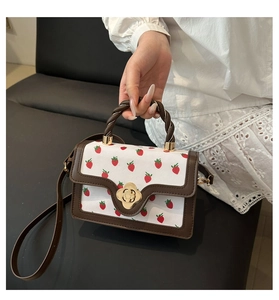 Close-up of golden flower turn-lock and strawberry print on vintage white leather handbag